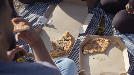 people taking pizza pieces from carton boxes on blanket