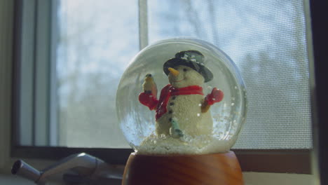 Schneeflocken-Setzen-Sich-In-Einer-Schneekugel-Ab,-Die-Tagsüber-In-Einem-Fenster-Steht