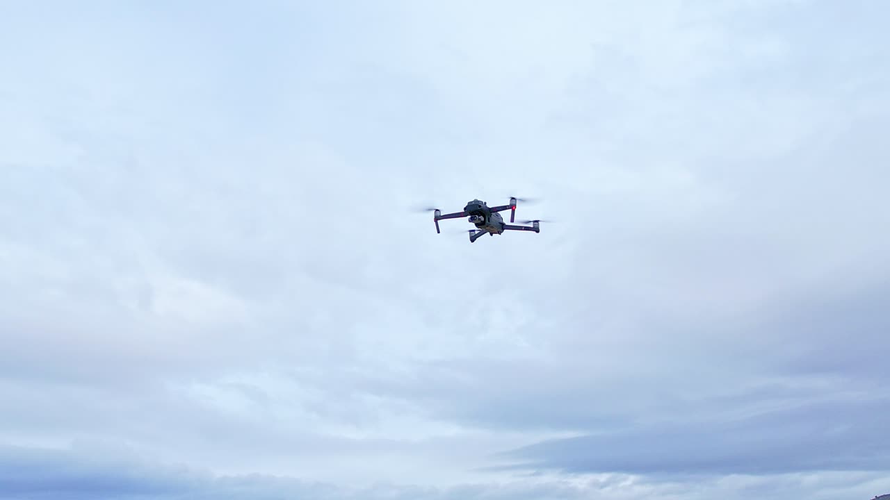 Drone in flight with position lights and signal flashes. Close aerial view. Drone flying with cloudy sky in the background.