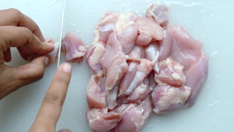 Hand-cutting-raw-breast-chicken-meat-on-chopping-board
