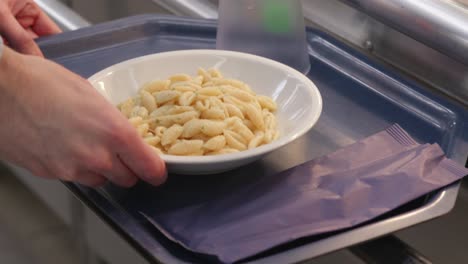 hands placing a fresh pasta dish onto a tray in food self-service line.