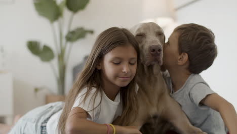 glückliche schwester und bruder umarmen und küssen ihren süßen hund zu hause, während sie in die kamera schauen