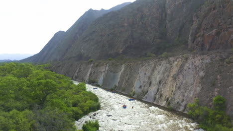 aerial - epic shot of kayaks on a river next to high mountain cliffs, forward