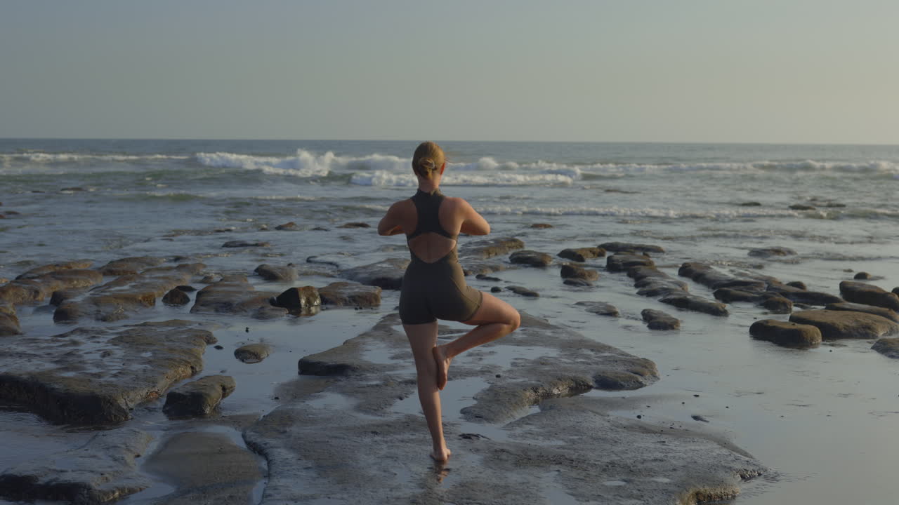 Donna che fa yoga su una spiaggia rocciosa