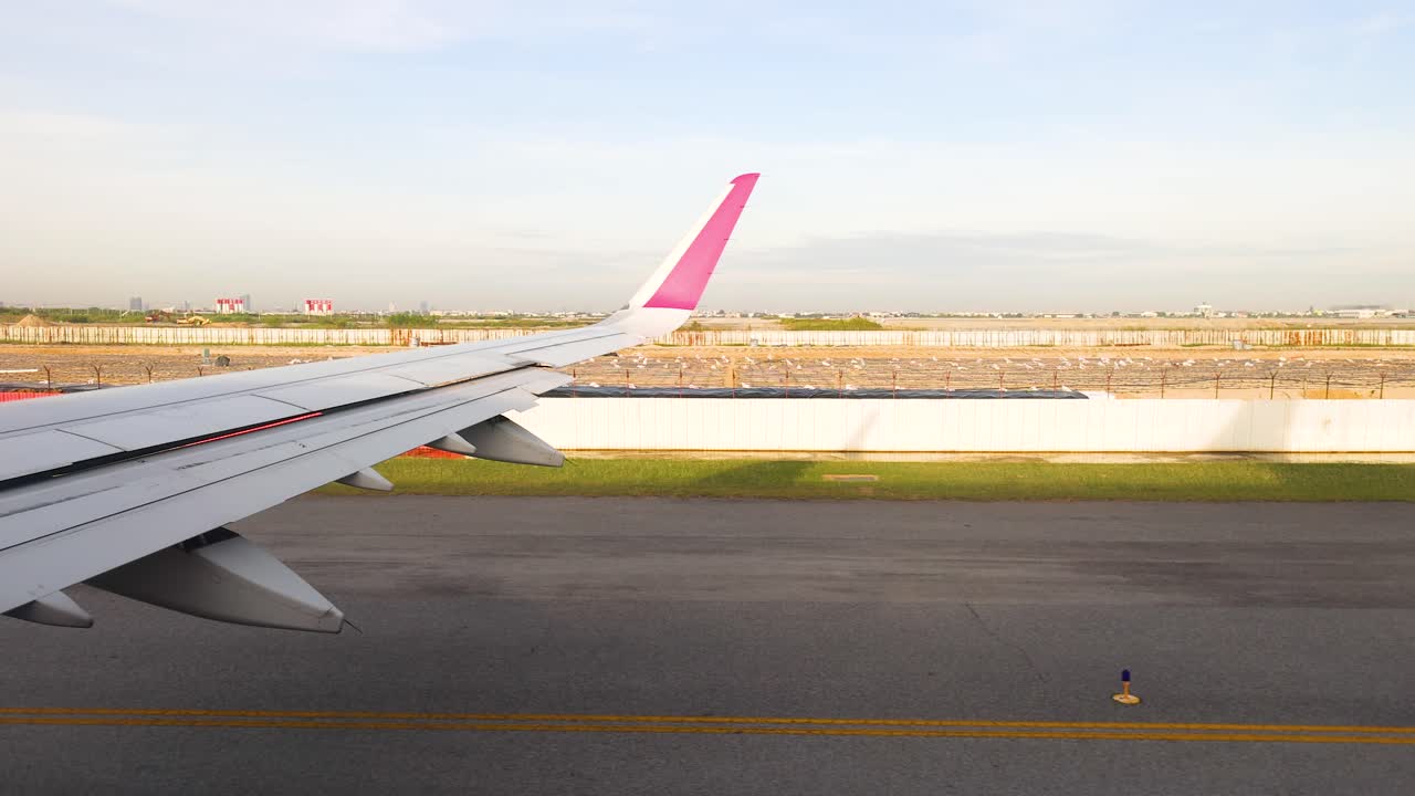 un taxi de avión en una pista de aterrizaje en un aeropuerto tailandés, mostrando su ala y el paisaje circundante a la luz del día