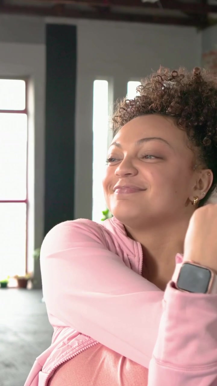 Vertical video: Crossing arms woman hugging, rolling, tilting neck for calm in loft in pink hoodie