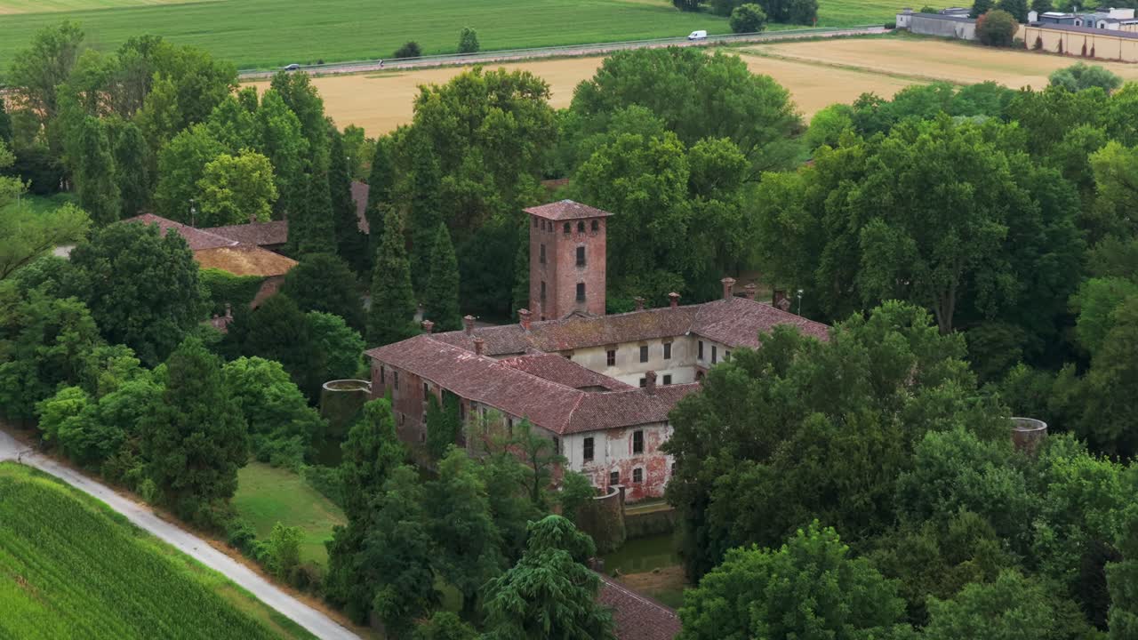 Borromeo Castle and moat in Peschiera Borromeo, near Milan, surrounded by lush trees and fields, Italy. Aerial backward