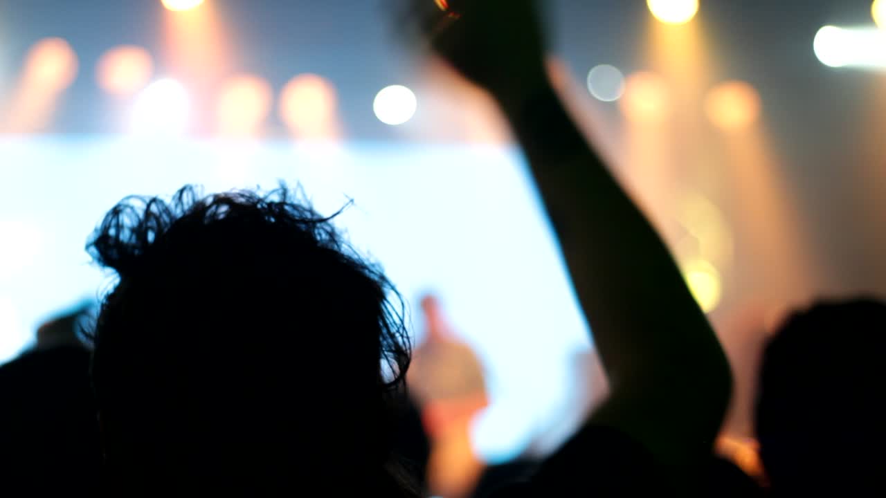 Uomo che alza le braccia e celebra canzoni da festa sul palco. Silhouette di un uomo di notte con retroilluminazione lampeggiante.