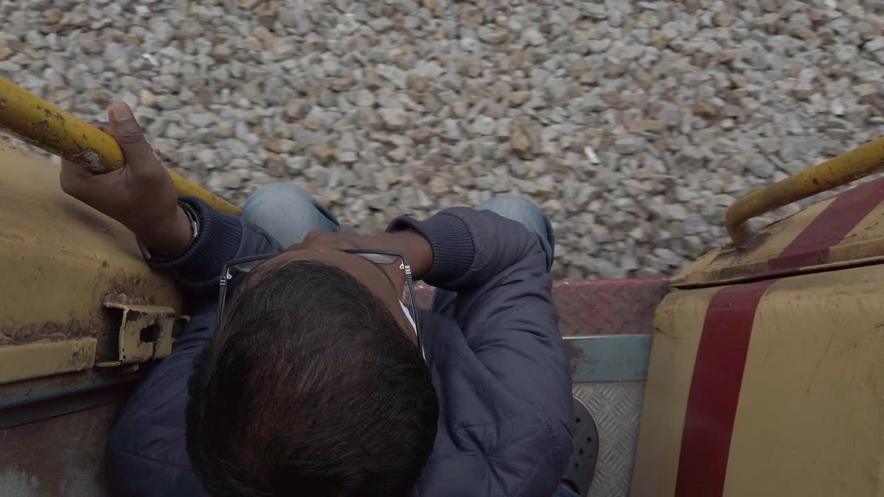 달리는 기차 안에서 기차 칸의 출구 문에 앉아 있는 남자의 모습을 내려다보고 있다