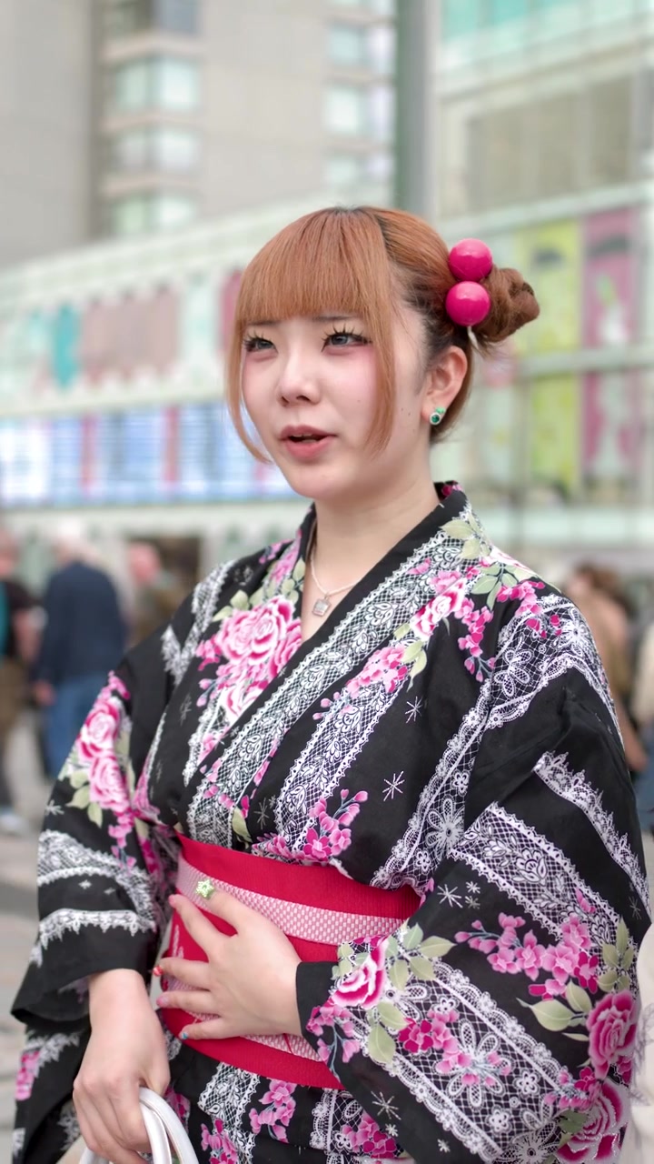 Una giovane donna che indossa uno yukata floreale è in piedi all'aperto in un'area affollata di un parco cittadino