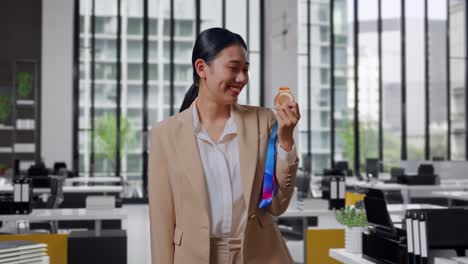 asian business woman in a suit kissing a gold medal in her hand being proud winning as the first winner in the office