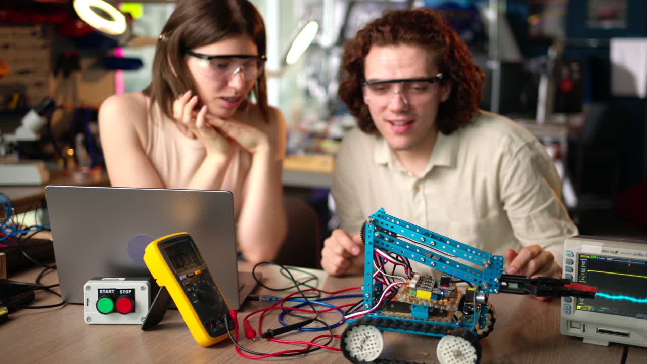 Two young happy engineers fixing a mechanical robot car in the workshop, computer programming