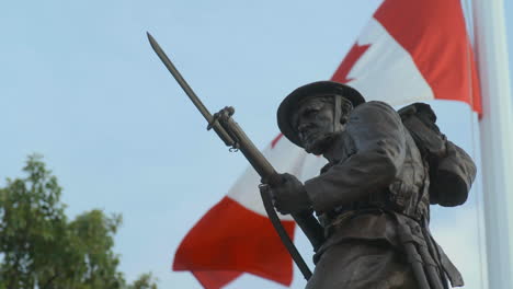 Estatua-De-La-Estatua-Del-Soldado-Canadiense-Wwi-Con-La-Bandera-Canadiense-En-Cámara-Lenta-Detrás,-En-Victoria-Bc