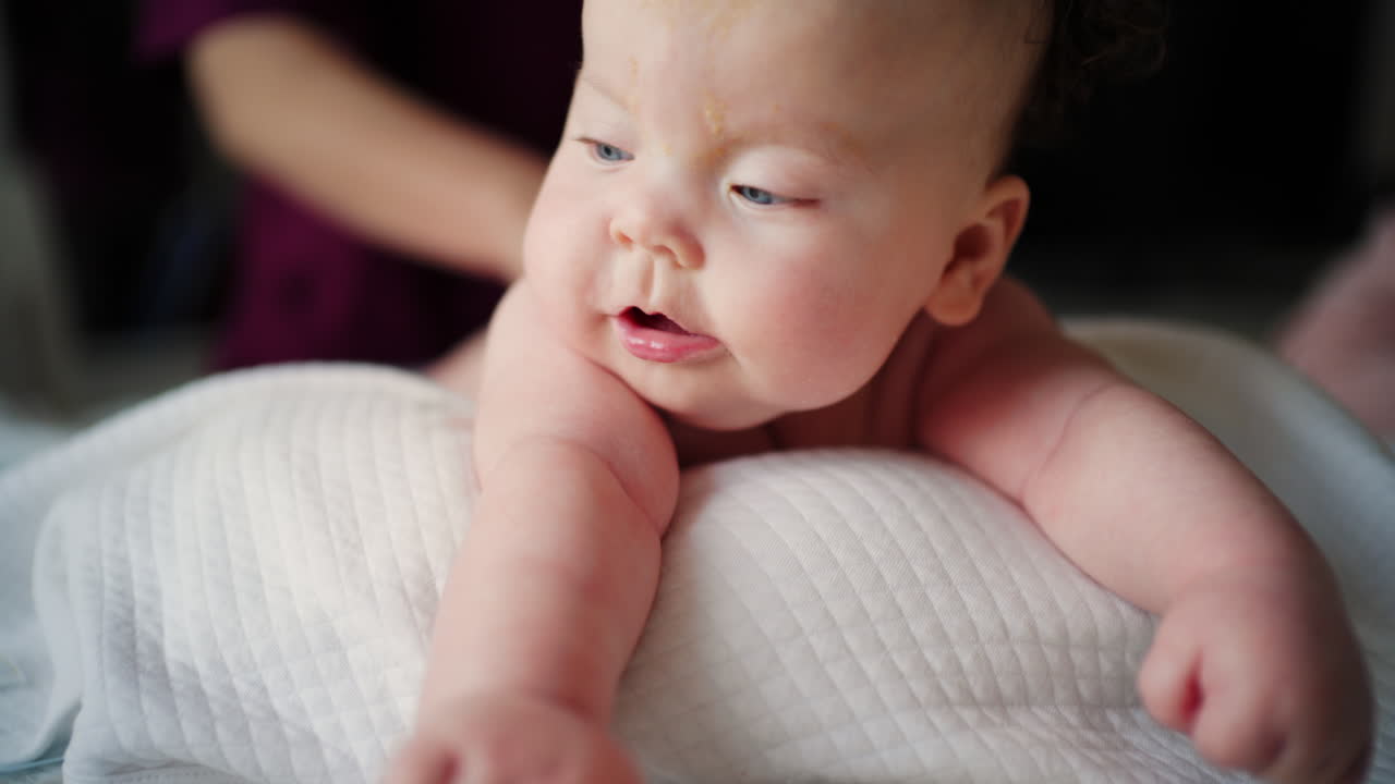 Caregiver gently stretching a baby's arms while the infant lies on a padded surface