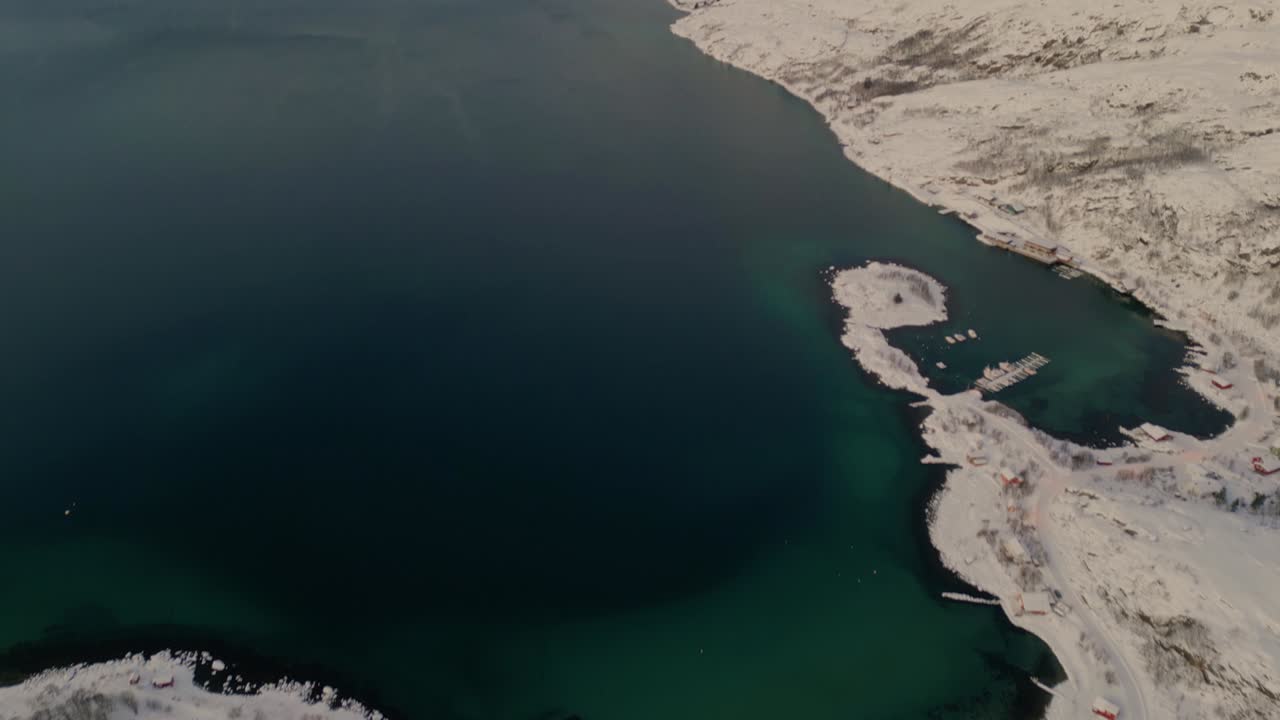 Vista aerea panoramica da un villaggio costiero innevato alle splendide acque color smeraldo dei fiordi.