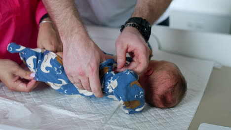 male and female hands putting a romper on a newborn child. parents caring together about their infant. close up.