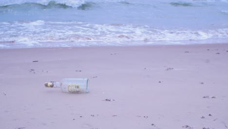 empty glass bottle on the beach, trash and waste litter on an empty and clean baltic sea white sand beach, environmental pollution problem, overcast day, medium shot