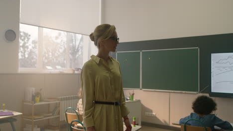 teacher walking in classroom with children. students doing test at lesson