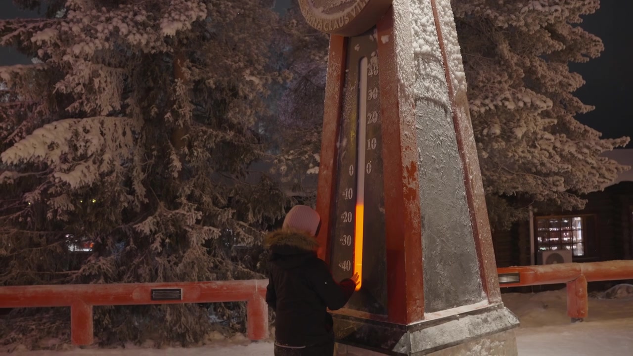 Lapsi koskettaa suurta ulkolämpömittaria lumisessa Joulupukin Pajakylässä.