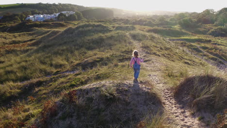 Drohnenaufnahme-Eines-Jungen-Mädchens-Im-Strandurlaub,-Das-In-Sanddünen-Vor-Der-Flackernden-Sonne-Spielt