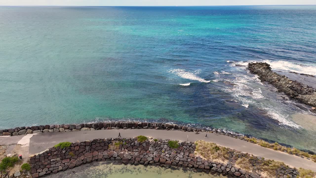Drone footage captures Apollo Bay's scenic coastal road and ocean waves under clear skies, showcasing the natural beauty of Victoria, Australia