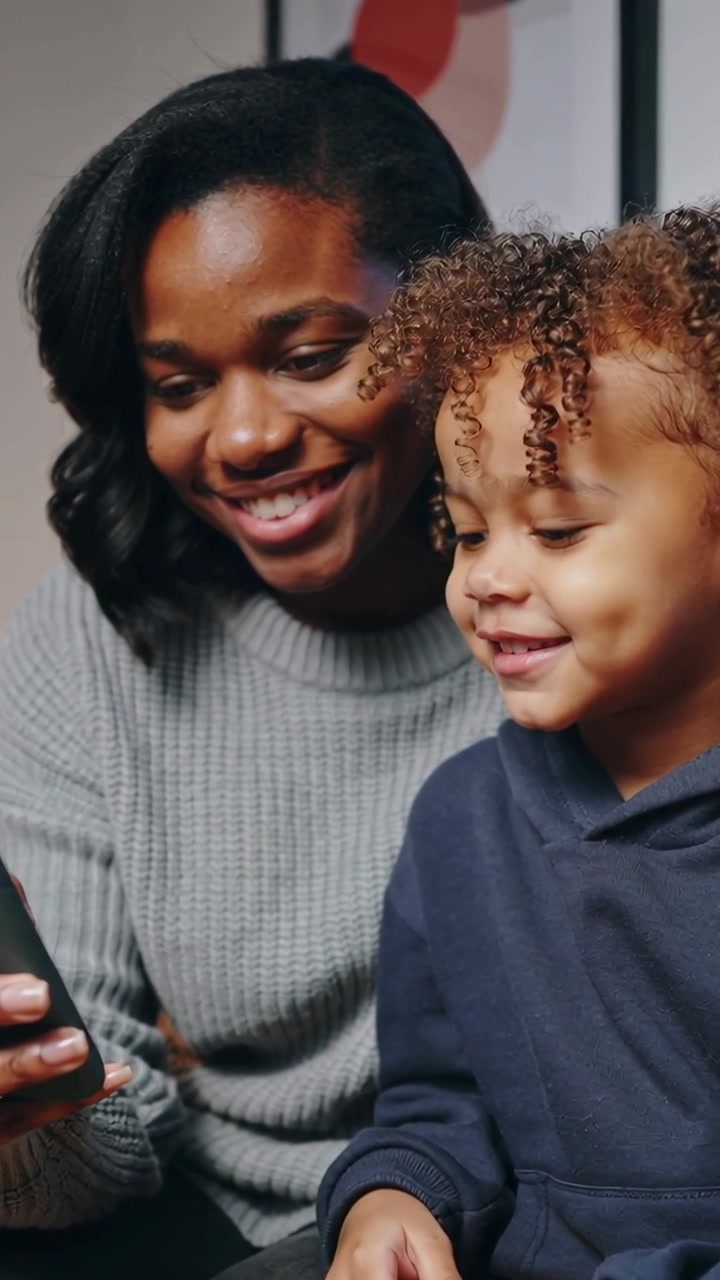 Vertical video: Angling phone, woman in grey sweater scrolling while child watching for fun on sofa