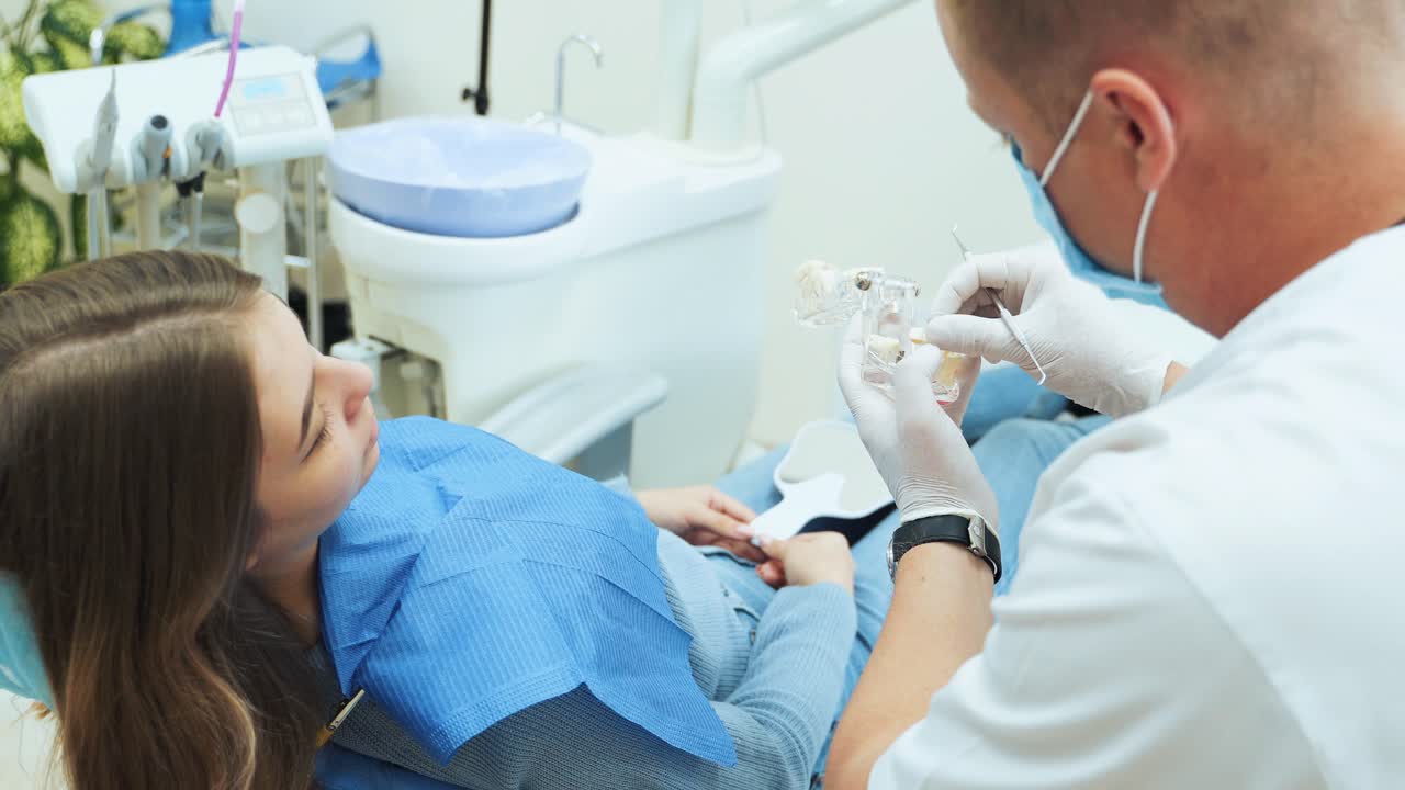 The dentist shows the patient a mock dentition with removable dentures and pins