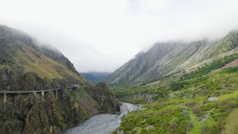 Truck-on-cliffside-road-through-mountain-landscape,-aerial