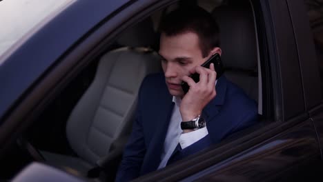 close-up of a man sitting in the car on a driver's seat, holding a smartphone. businessman talking while sitting in a car