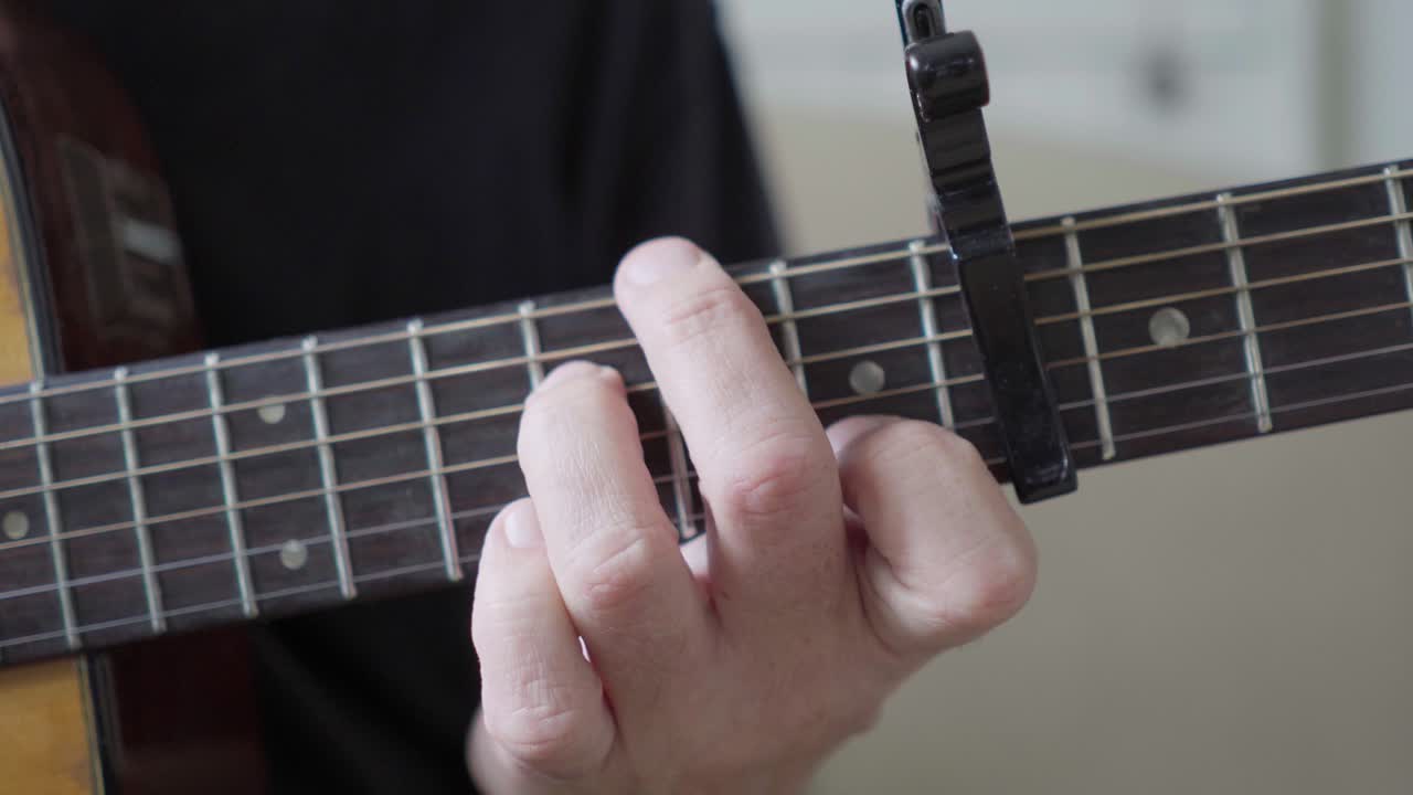A guitarist's left hand playing an acoustic steel-string guitar