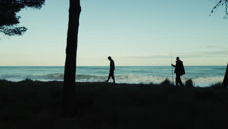 two people silhouette walking on the shore in front of a stormy ocean waves