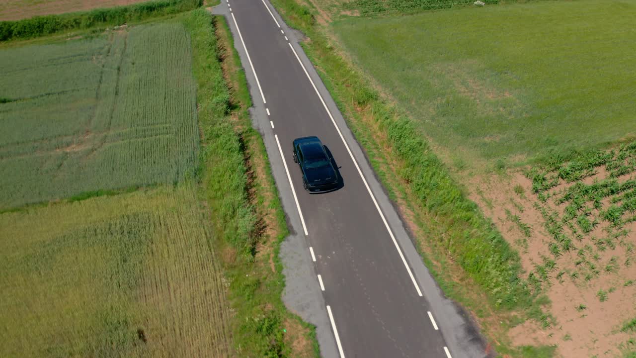A captivating drone shot orbiting a moving Dodge Challenger Scat Pack while simultaneously pulling back, revealing the vast rural landscape.