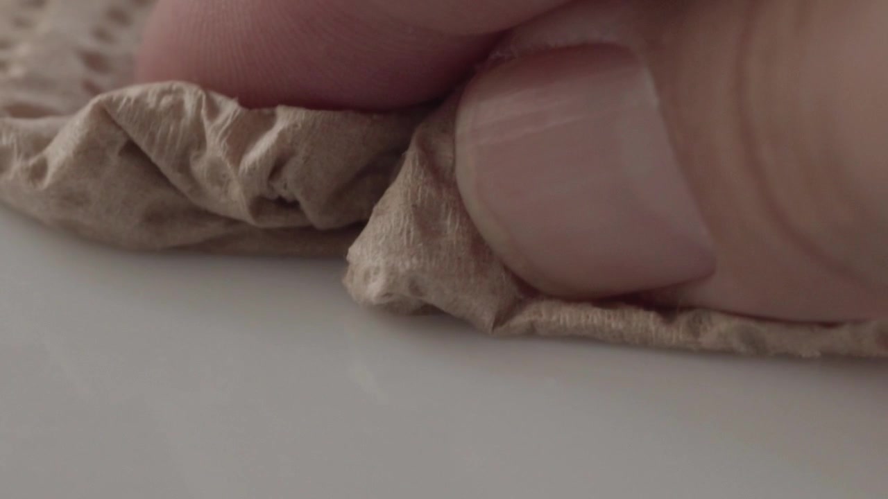 Primer plano macro de una mano limpiando una superficie blanca con un paño de limpieza suave. La presión suave elimina los residuos mientras la tela se desliza suavemente, destacando la limpieza diaria y el cuidado de superficies