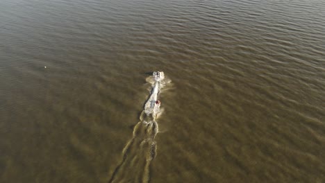 Toma-De-Seguimiento-Aéreo-En-Cámara-Lenta-De-4k30-De-Una-Moto-De-Agua-Tomando-Un-Remolcable-Inflable-Al-Atardecer-En-Uruguay,-Sudamérica