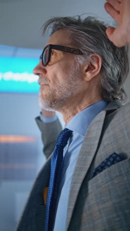 older man in suit, looking away, hands raised