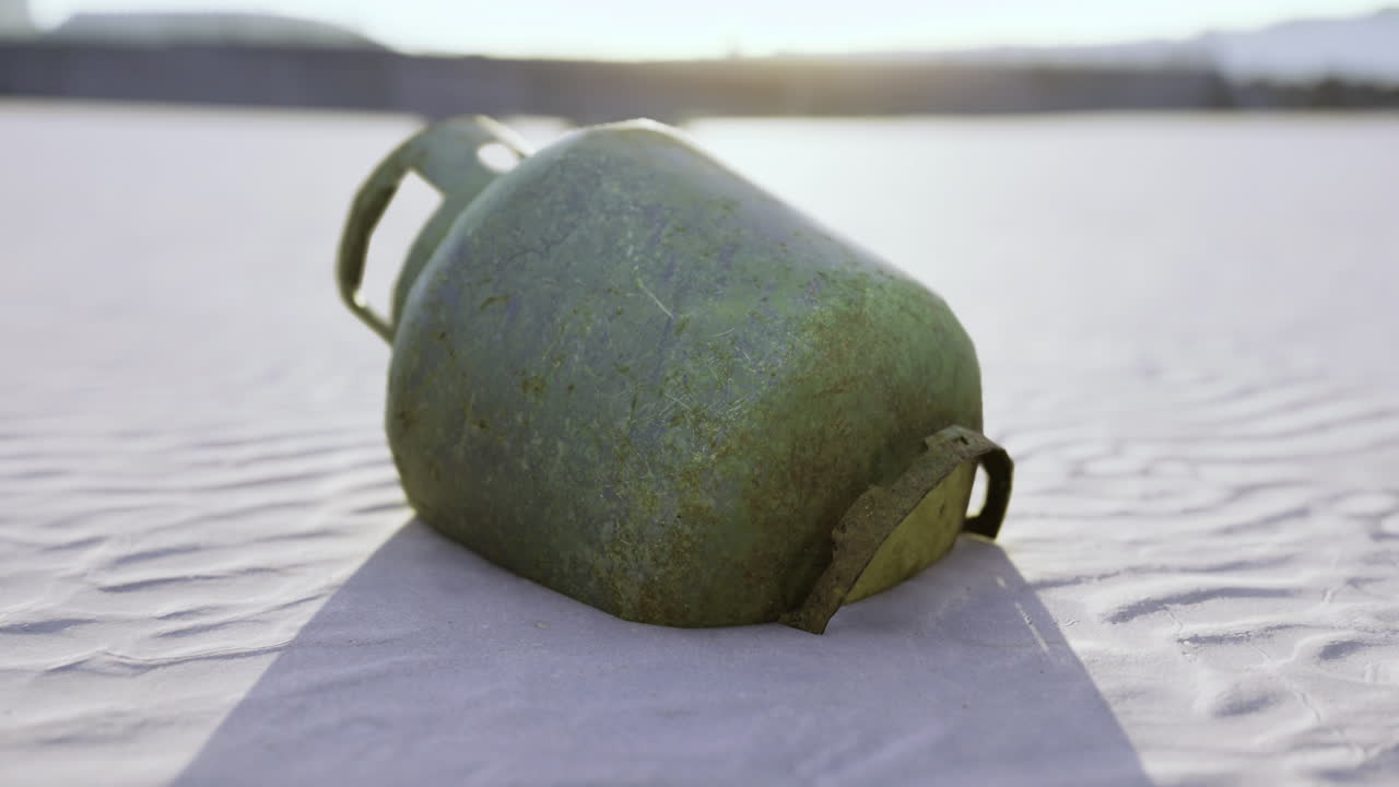 Forgotten gas tank rests on sunlit desert sand at dusk with soft shadows