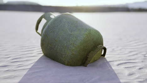 forgotten gas tank rests on sunlit desert sand at dusk with soft shadows