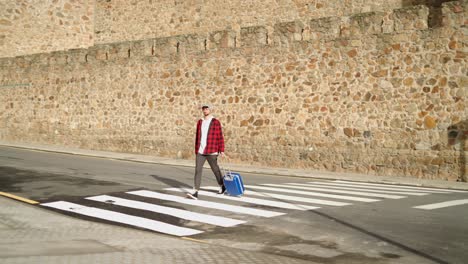 male traveler crossing a crosswalk with his luggage