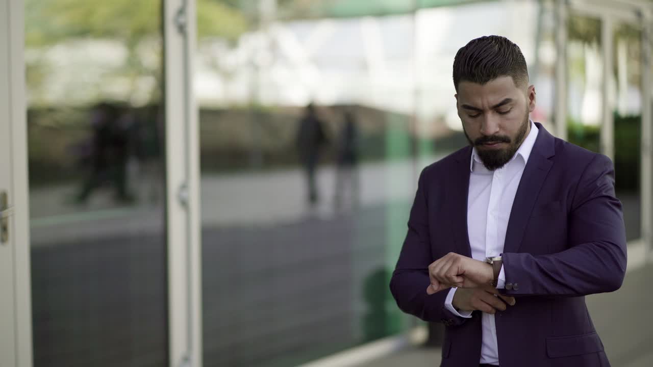 Serious businessman checking wrist watch on street