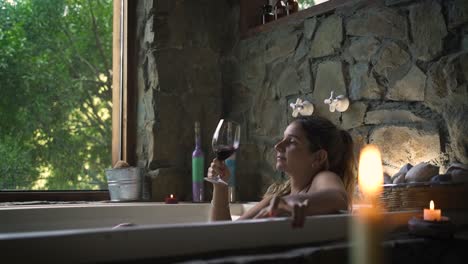 Mujer-Joven-Y-Atractiva-Que-Tiene-Un-Baño-De-Lujo-En-Un-Jacuzzi-Bebiendo-Vino-Con-Una-Gran-Ventana-Verde-De-La-Naturaleza-Capaz-De-Cámara-Lenta-60fps