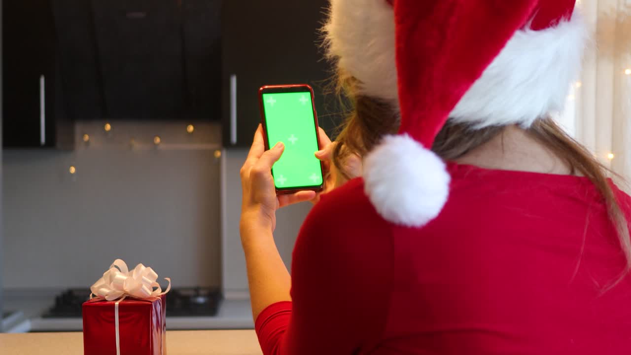 부에서 새해의 빨간색 슈트를 입은 소녀가 손가락으로 녹색 화면을 가진 스마트폰을 통해 잎을