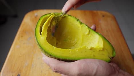 scooping ripe avocado flesh with spoon, close up