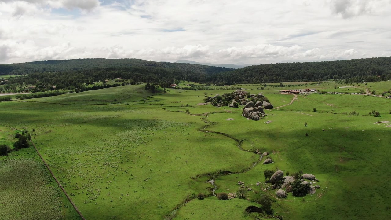 Ampio paesaggio aereo vicino alle rocce di granito Las Piedrotas con prati verdi, ruscello tortuoso e ombre di nuvole in movimento a Tapalpa