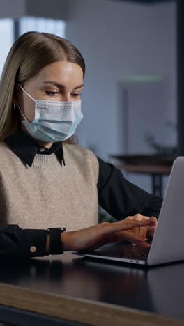 businesswoman in mask working with laptop. quarantine freelancer working on workplace. vertical video