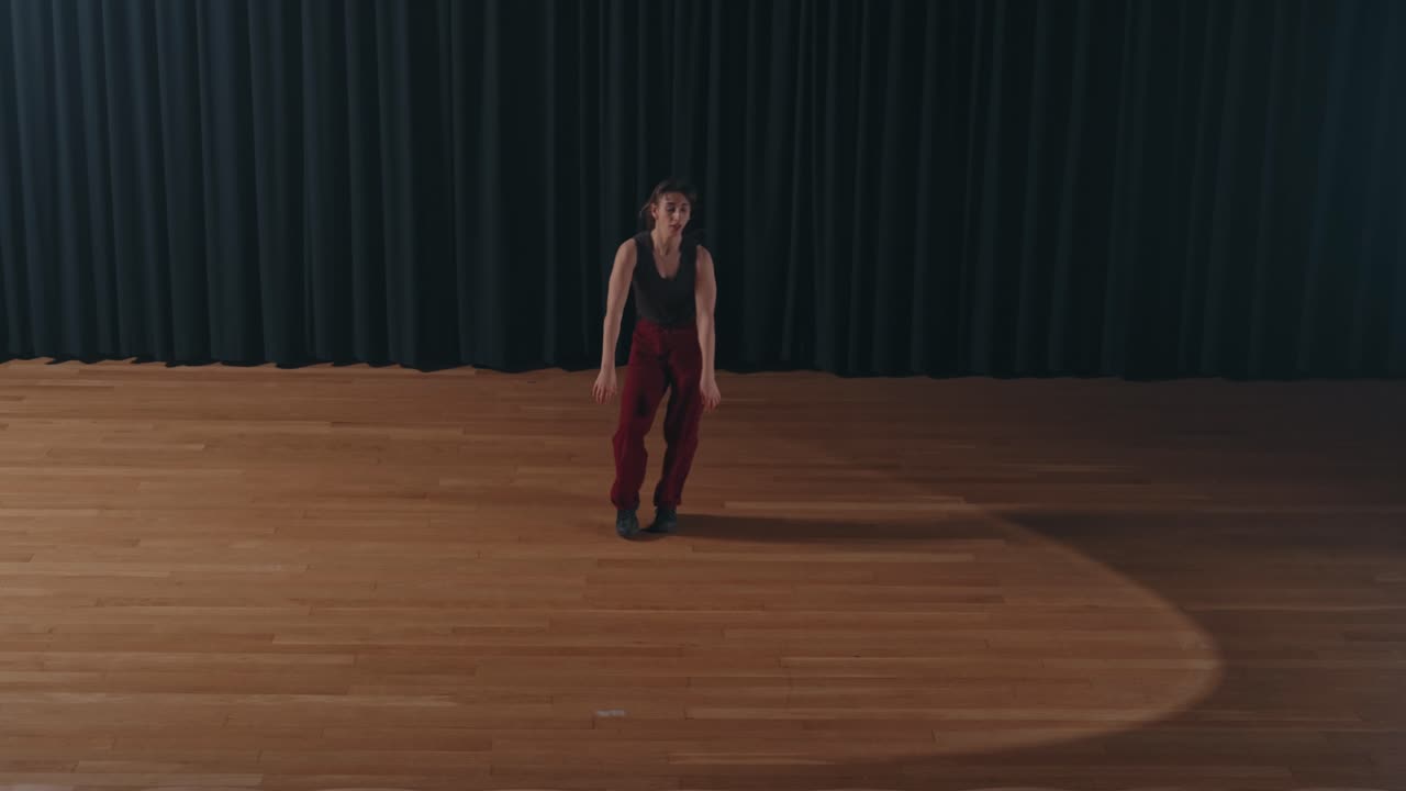 Ballerino solista in pantaloni rossi si muove dinamicamente su un palco di legno davanti a un sipario scuro.