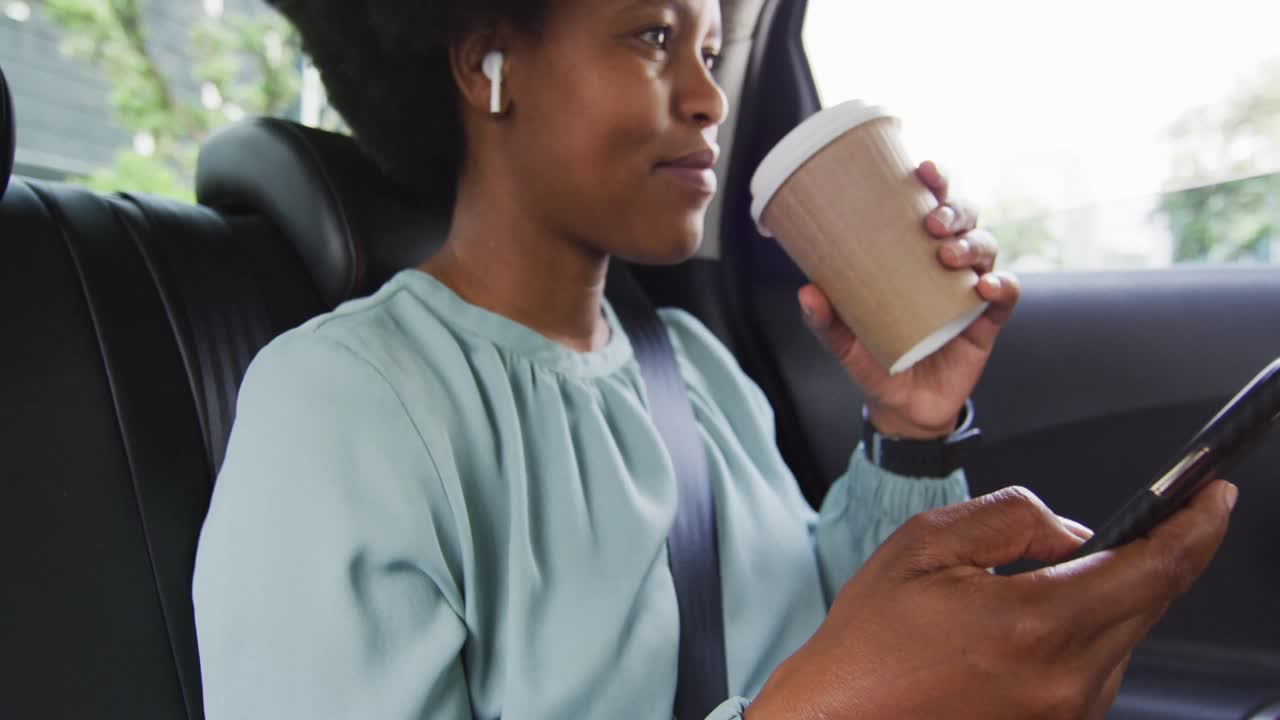 African american businesswoman using smartphone and holding takeaway coffee in car