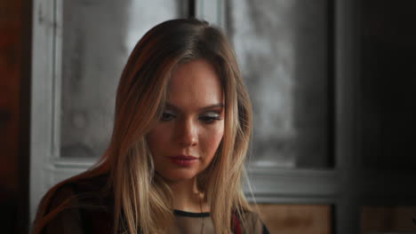 mujer joven sentada en una cafetería en una mesa de madera, bebiendo café y usando un teléfono inteligente. en la mesa hay una computadora portátil. chica navegando por internet, chateando, blogueando. mujer sosteniendo el teléfono y mirando su pantalla.