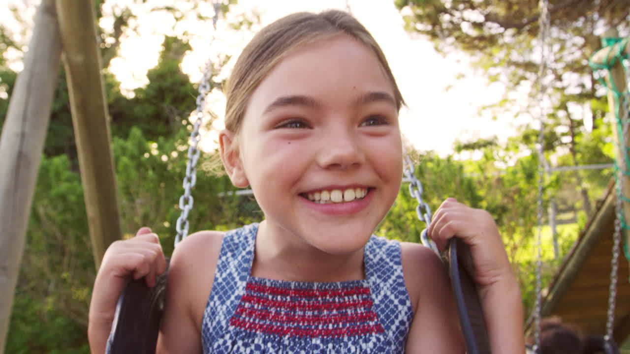 Two Girls Playing Outdoors At Home On Garden Swings