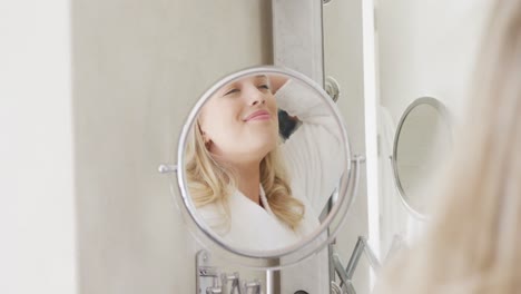 mujer caucásica feliz de talla grande con bata de baño y cepillándose el cabello en el baño en cámara lenta