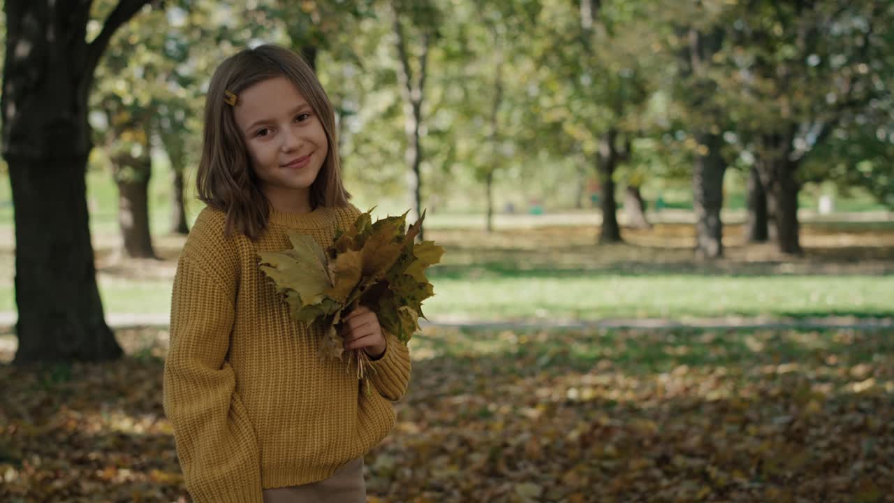 Portrait of smiling little girl with bouquet of autumn's leaves.